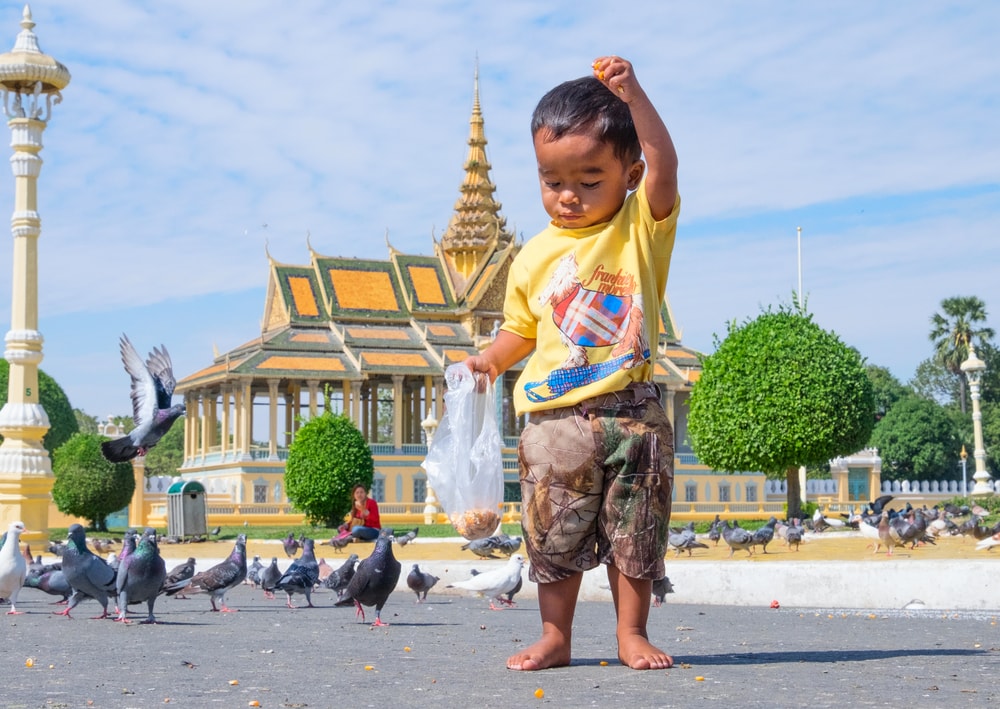 Niño dando de comer a las palomas, descalzo en Phnom Penh